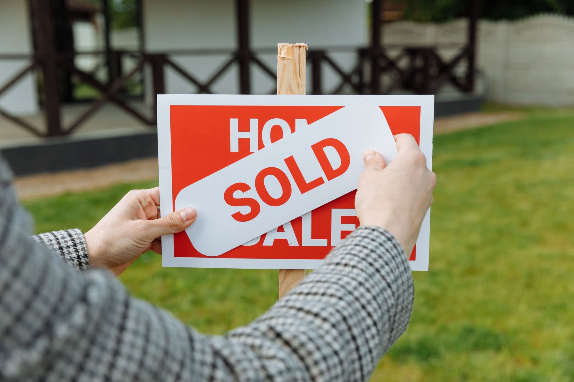 Close-up of hands placing a sold sticker on a real estate sign outside a house.